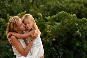 Mother hugging her little daughter outdoors, showing love, tenderness and emotional family bond in...