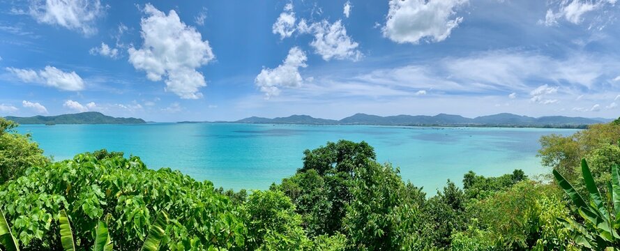 Scenic panoramic view of Phuket Island from Khao Khad viewpoint. Lush tropical trees, turquoise sea, and coastal landscape under clear sky. Tranquil and exotic atmosphere
