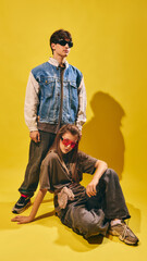 Young man and woman in oversized streetwear with sunglasses on yellow backdrop. Concept of Gen Z...