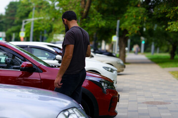 Man inspecting a red car in a parking lot surrounded by other vehicles on a sunny day © Nariman
