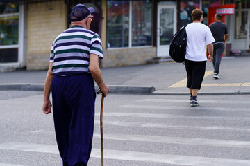 Elderly man with cane crossing street while younger man walks away in urban setting during daytime