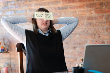 Lazy unproductive young guy wearing funny sticky notes with open eyes on his glasses, sleeping at...