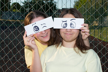 Portrait of a two young women with a funny drawn paper eyes	