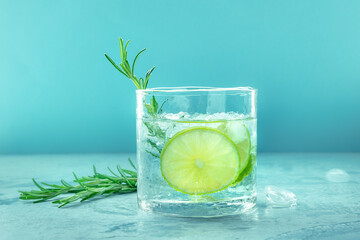 Gin tonic glass, side view with rosemary and lime. Fresh summer cocktail with ice on a blue background