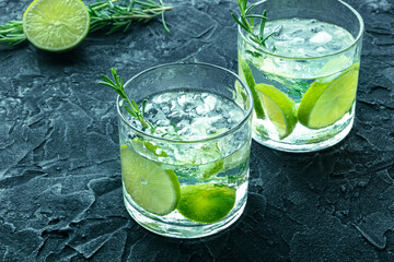 Gin tonic, two glasses of gin with soda, lime, rosemary, and plenty of ice, on black, fresh summer cocktail on a black background