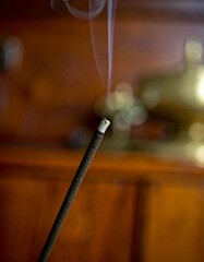 Macro close-up of burning incense stick with delicate swirls of thin white smoke rising gracefully, spiritual and meditative ambiance, warm blurred background