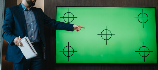 A business professional gesturing toward a green screen with target symbols, illustrating a presentation or demonstration.