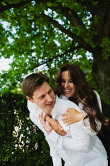Loving married couple shares a joyful moment outdoors, embracing each other amidst vibrant green trees and warm sunlight