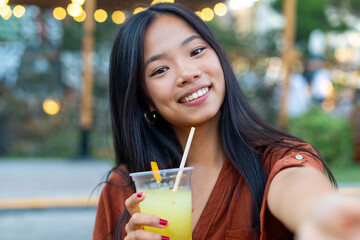 Young woman taking a selfie while enjoying a refreshing drink outdoors