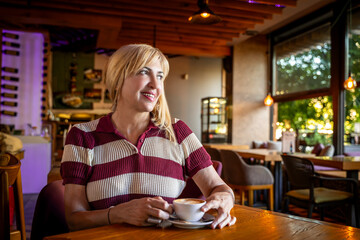 Portrait of senior female enjoying in restaurant, waiting for lunch, drinking coffee. Attractive mature woman sitting in bar, enjoying in beverage. 