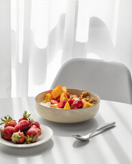 Granola or muesli with natural greek yogurt, strawberry and peach in a bowl on a white table near window