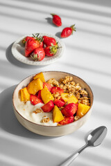 Granola or muesli with natural greek yogurt, strawberry and peach in a bowl on a white background