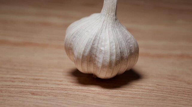Close-up of a garlic bulb on wooden surface, filmed with a rotating camera. Detailed view of texture and shape. Ideal for food content, cooking, ingredients, or natural product visuals.