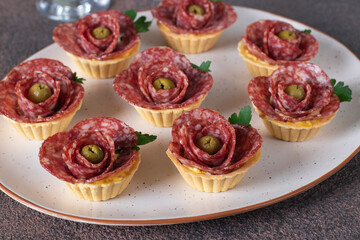 Tartlets in shape of roses with sausage salami and olives on white plate