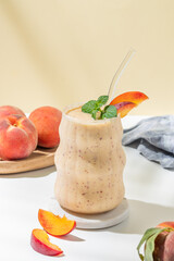 Smoothie with peach and banana in a glass on a marble stand on a yellow white background with...