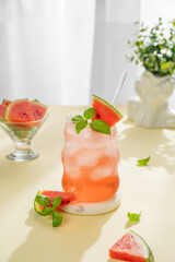 Watermelon mojito cocktail with ice and mint in a glass on a marble stand on a yellow table near window