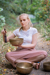 Young woman in sound healing session in nature with Tibetan singing bowls