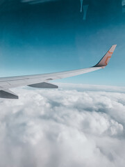 Airplane wing cutting through bright blue sky above fluffy clouds — classic view from a peaceful flight.