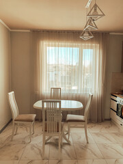  Bright minimalist dining room with a round table and white chairs, sunlight streaming through sheer curtains.