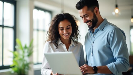 Two colleagues smiling while looking at a laptop screen in a bright and modern office space setting