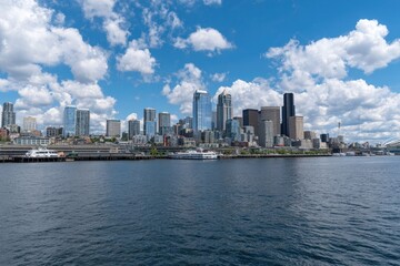 Fototapeta premium Wide shot of Seattle skyline from across the water, featuring modern skyscrapers, waterfront, and puffy clouds