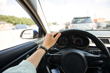 A woman's hand with a watch holds a car steering wheel. Traffic jam on the road.
