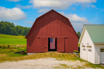 Obraz premium A rustic barn on a hill in a rural New England village, proudly displaying an American flag, embodies the region’s heritage and timeless countryside charm.