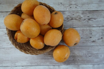 Fresh loquats overflowing a rustic woven basket on wooden table
