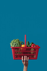 A hand lifting up a shopping basket with fresh veggies. Space for text. 