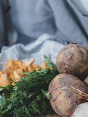 Close-up composition of raw potatoes, fresh chanterelle mushrooms, parsley, dill, and green onions arranged on a wooden board with a striped kitchen towel.