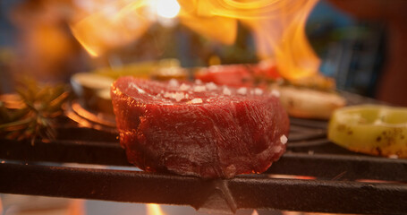 Grilling seasoned steak with vegetables over flames on barbecue grill