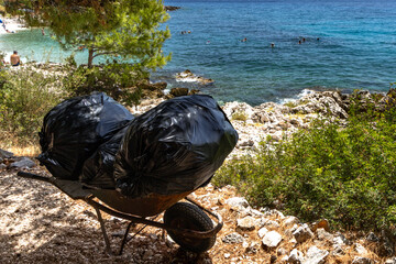 Black garbage bags collected on the beach, beach waste removed in a wheelbarrow, beach waste...