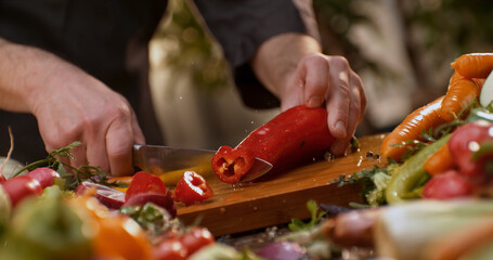 Chef cutting red pepper on wooden board, surrounded by fresh vegetables