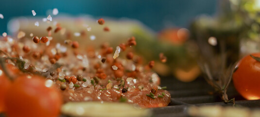 Seasoning falling on hamburger meat grilling with vegetables and tomatoes