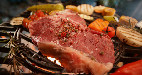 Grilling seasoned t-bone steak and vegetables on barbecue grill
