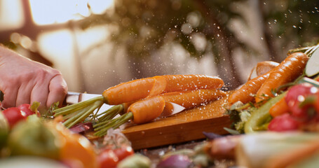 Chef cutting fresh carrots on wooden board, surrounded by vegetables