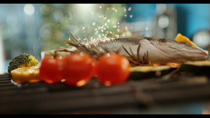 Chef sprinkling salt on fresh sea bass grilling with vegetables