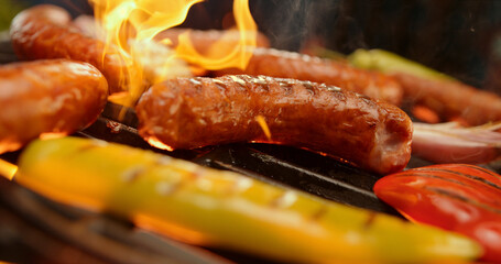Grilling sausages and vegetables on a flaming barbecue grill