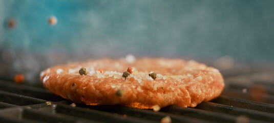 Burger patty grilling with salt and pepper falling on hot surface