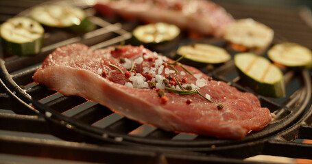 Grilling seasoned steak and zucchini on barbecue grill