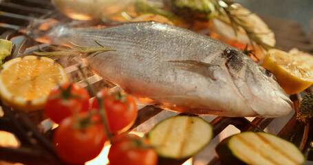 Dorado fish grilling with vegetables on barbecue grill