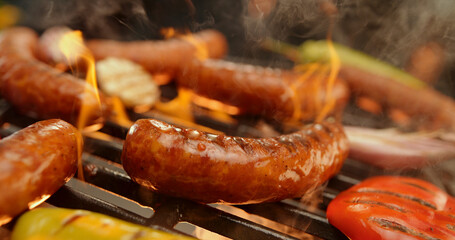 Delicious sausages and vegetables grilling on barbecue with flames