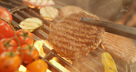 Chef grilling hamburgers and vegetables on flaming barbecue grill