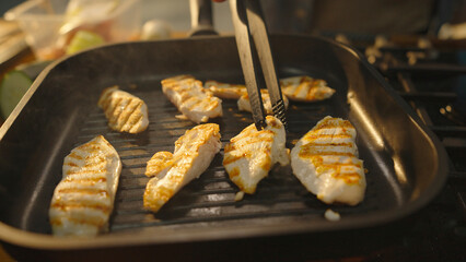 Chef turning chicken breast fillets with tongs on grill pan