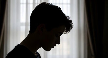 Silhouette of a young person looking down against a bright window