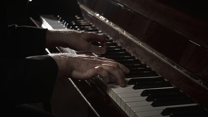 Close up male hands playing piano keys in dark studio light. Concept of music performance, jazz...