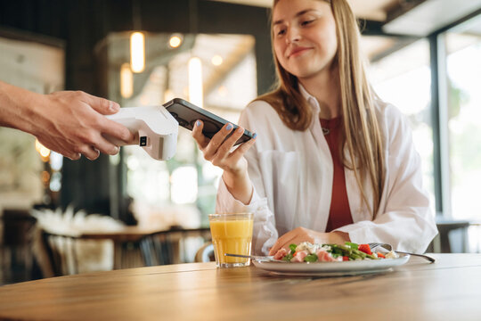 Laptop, salad and orange juice. Woman is paying for meal by wireless payment in the cafe restaurant