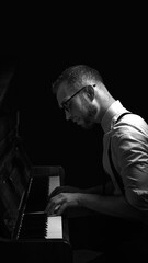 Man playing piano in dark moody lighting wearing glasses and suspenders. Concept of music performance, artistic expression, jazz concert, emotional stage presence.