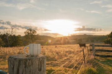 Coffee mug sitting on fence post on farm at sunrise