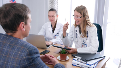 Fototapeta premium The happy doctor informs the patient about his excellent health. A woman in glasses and a white coat is talking to a patient in a medical office